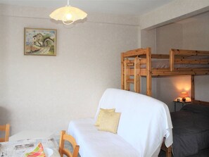 Ein Zimmer mit Etagenbett, einem Einzelbett, einem Tisch mit Stuhl, einem Wandbild und einer Pendelleuchte.