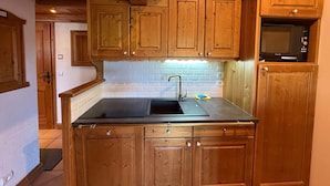 Una cocina con armarios de madera, encimera negra, un lavabo y un microondas.