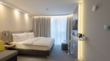 Een moderne hotelkamer met een groot bed, nachtkastje en een klein rond tafeltje met een stoel.
