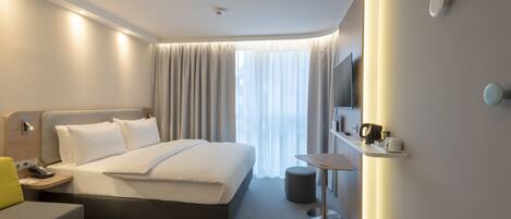 A modern hotel room with a large bed, bedside table, and a small round table with a chair.