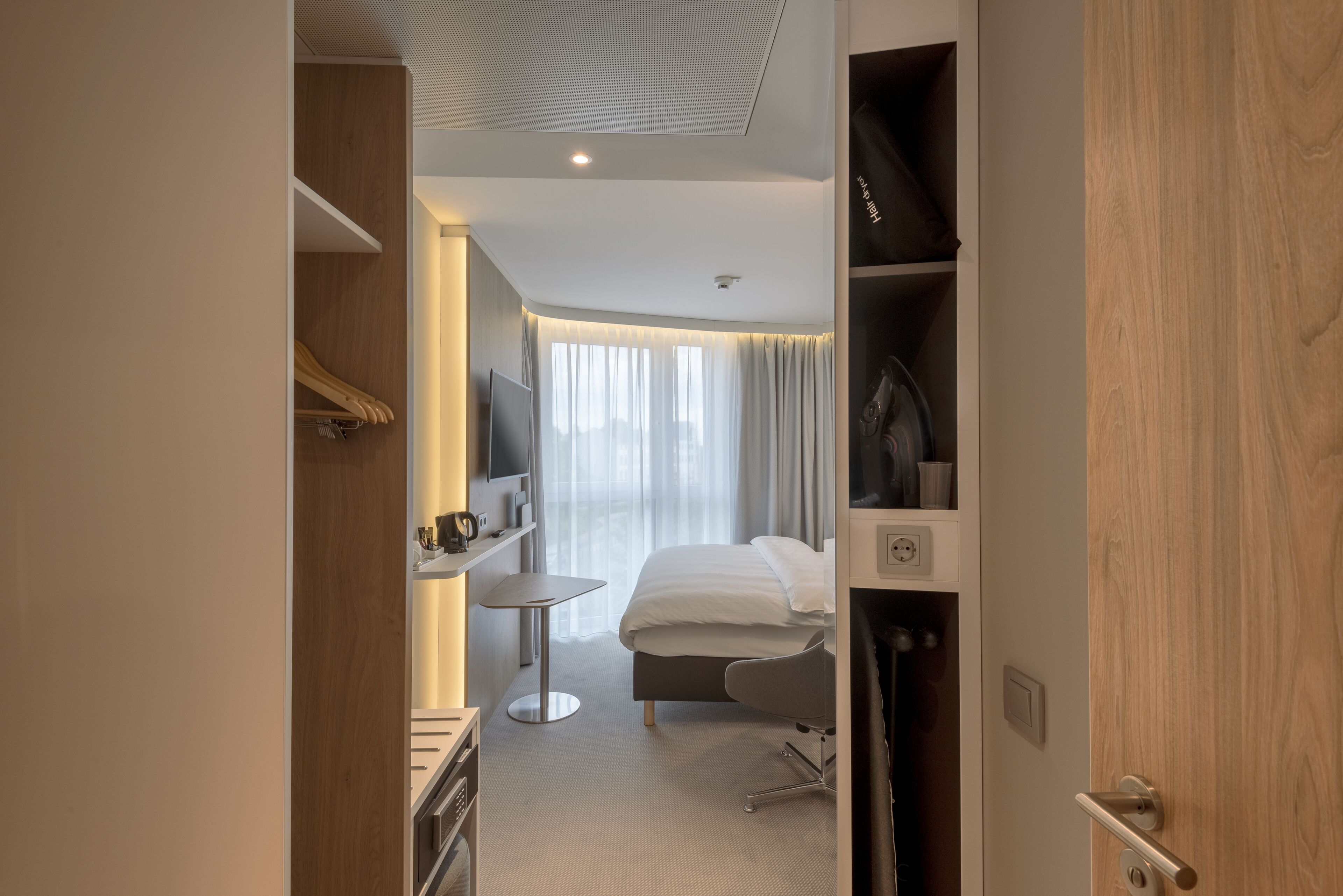 A hotel room with a bed, a desk, a chair, a TV, and a wardrobe.