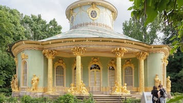 Un edificio histórico con columnas y estatuas doradas ornamentadas, que presenta una cúpula central y ventanas de arco.