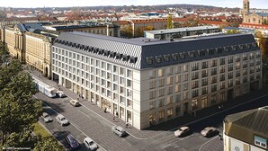 A modern building with a flat roof and large windows, surrounded by a cityscape with a prominent tower in the background. - Holiday Inn Express and Suites Potsdam by IHG (Potsdam)