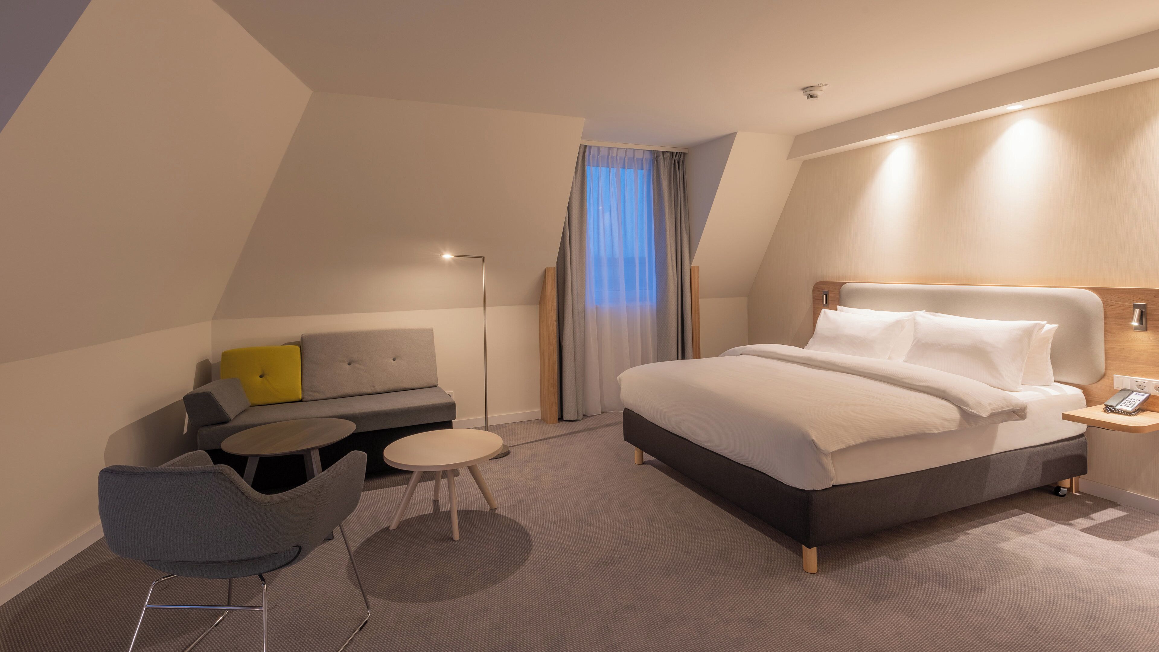 A modern hotel room with a bed, a sofa, a small table, and a chair.