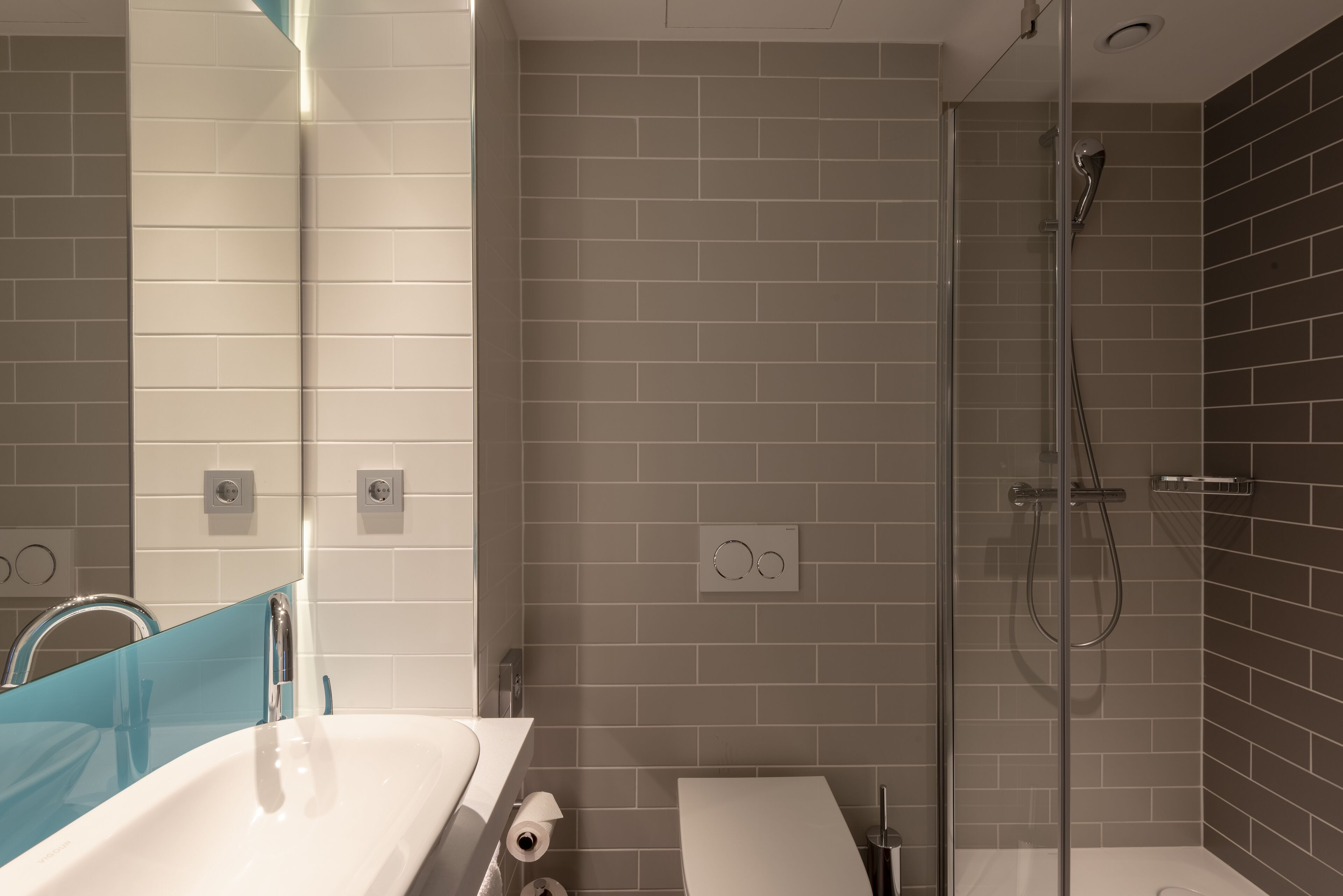 Une salle de bain moderne avec une douche à parois de verre, un lavabo blanc et un miroir agrémenté d’une touche de bleu.
