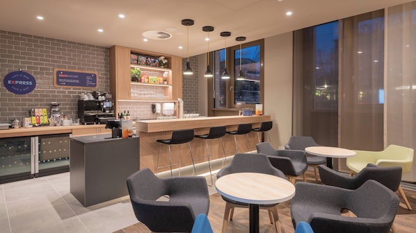 A modern cafe with a bar area, seating, and a view of the city at dusk. - Holiday Inn Express and Suites Potsdam by IHG (Potsdam)