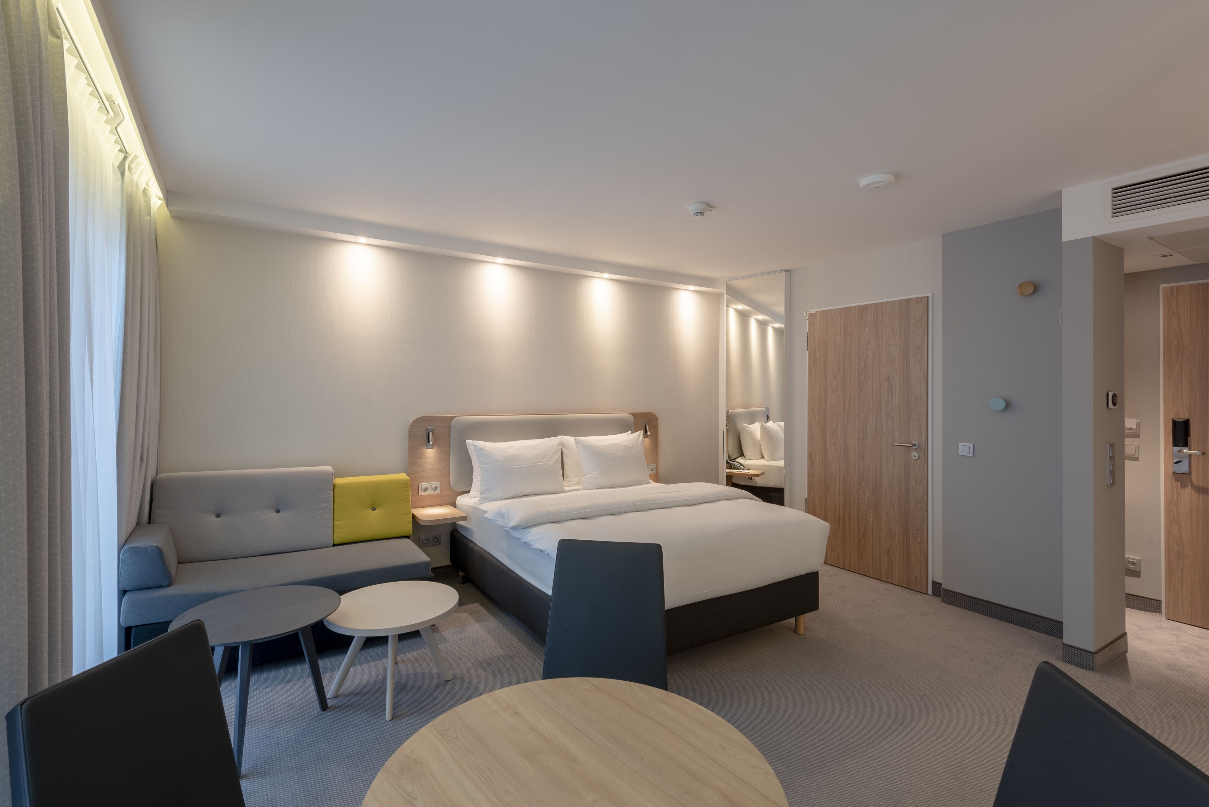 A modern hotel room with a bed, a sofa, a small table, and a chair.