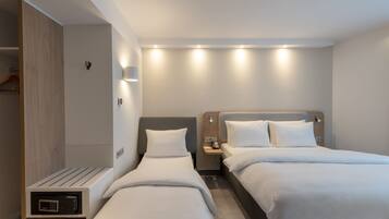 A modern hotel room with two beds, a bedside table with a phone, and a built-in TV.