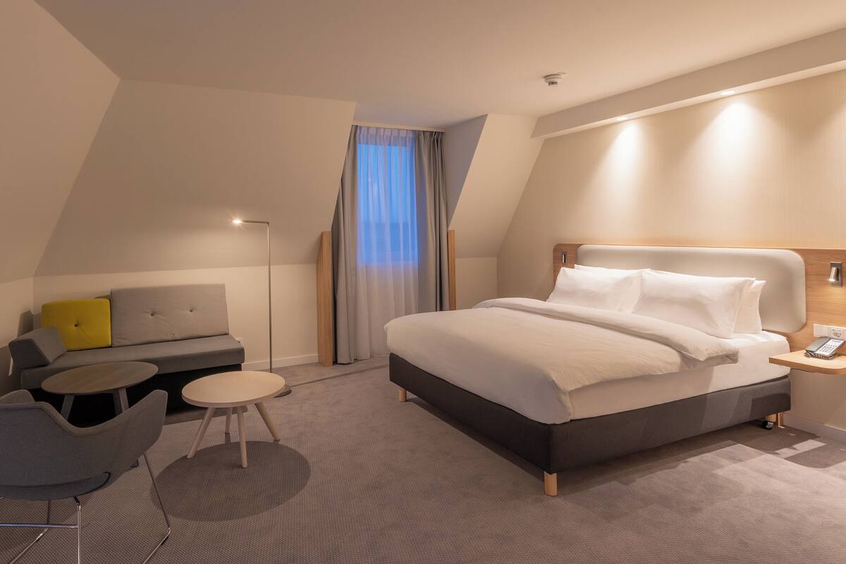 A modern hotel room with a bed, a sofa, a small table, and a chair.