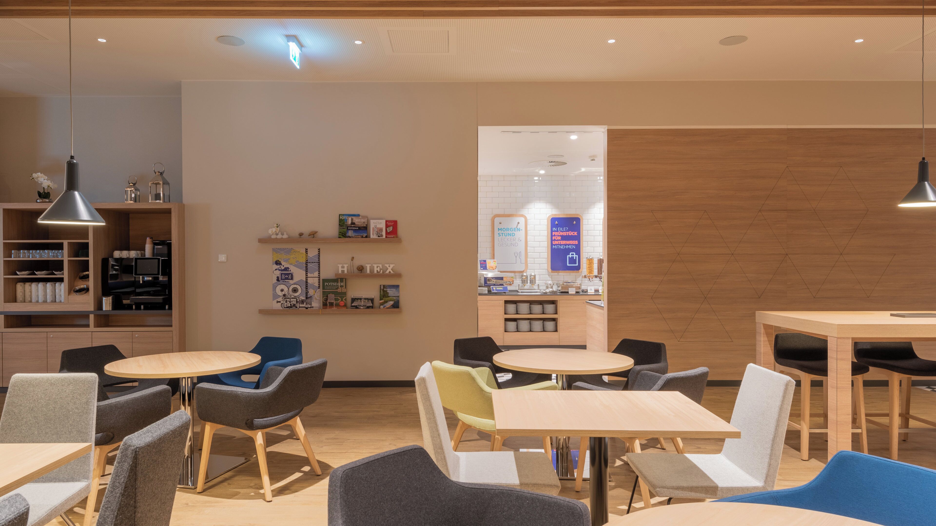 Una cafetería moderna con mesas y sillas redondas, una máquina de café y un panel con la carta.