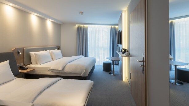 A hotel room with two beds, a desk, a chair, a small table, a mirror, and a wardrobe. - Holiday Inn Express and Suites Potsdam by IHG (Potsdam)