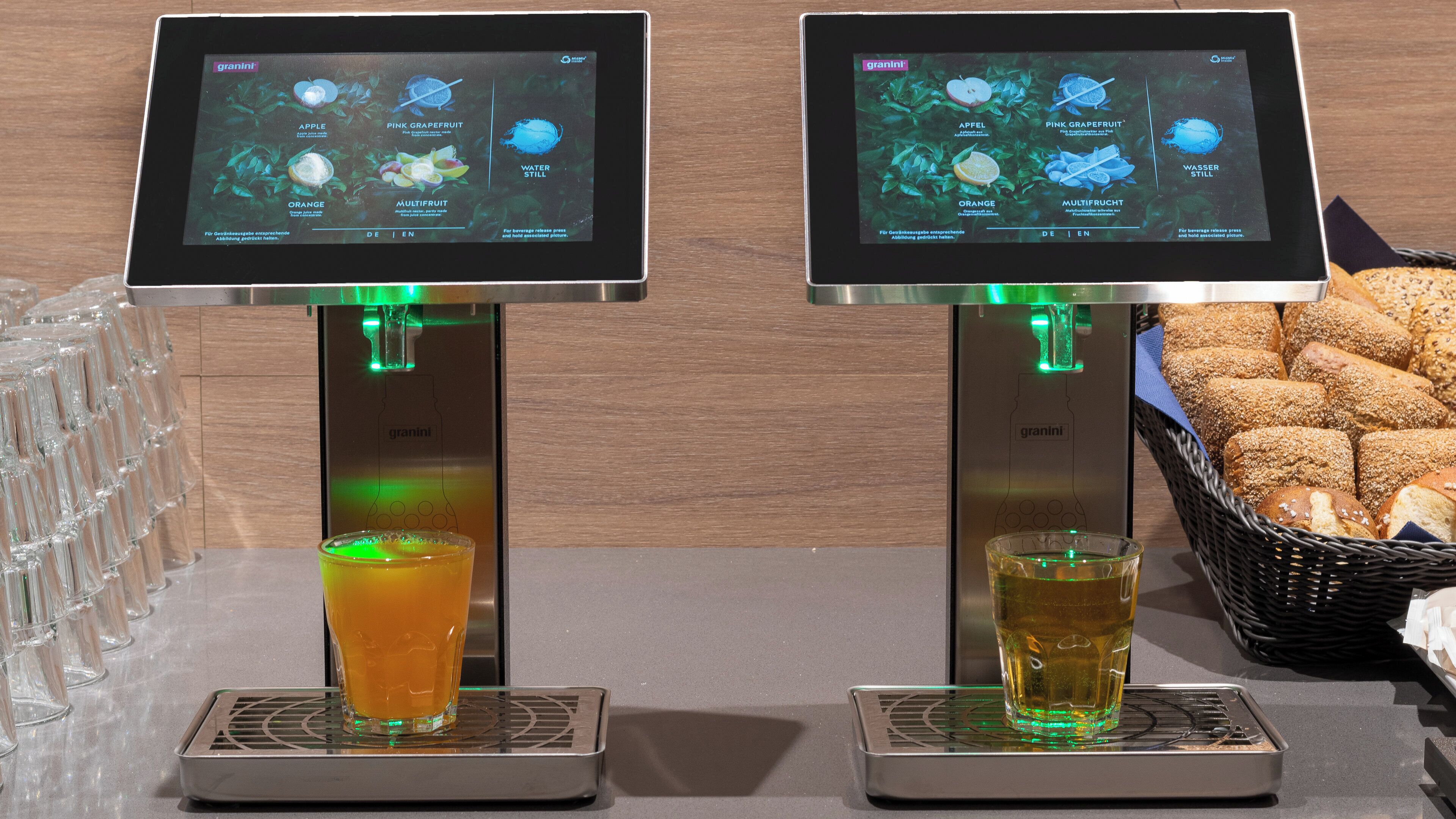 Two beverage dispensers with digital displays, glasses filled with drinks, and a basket of bread.