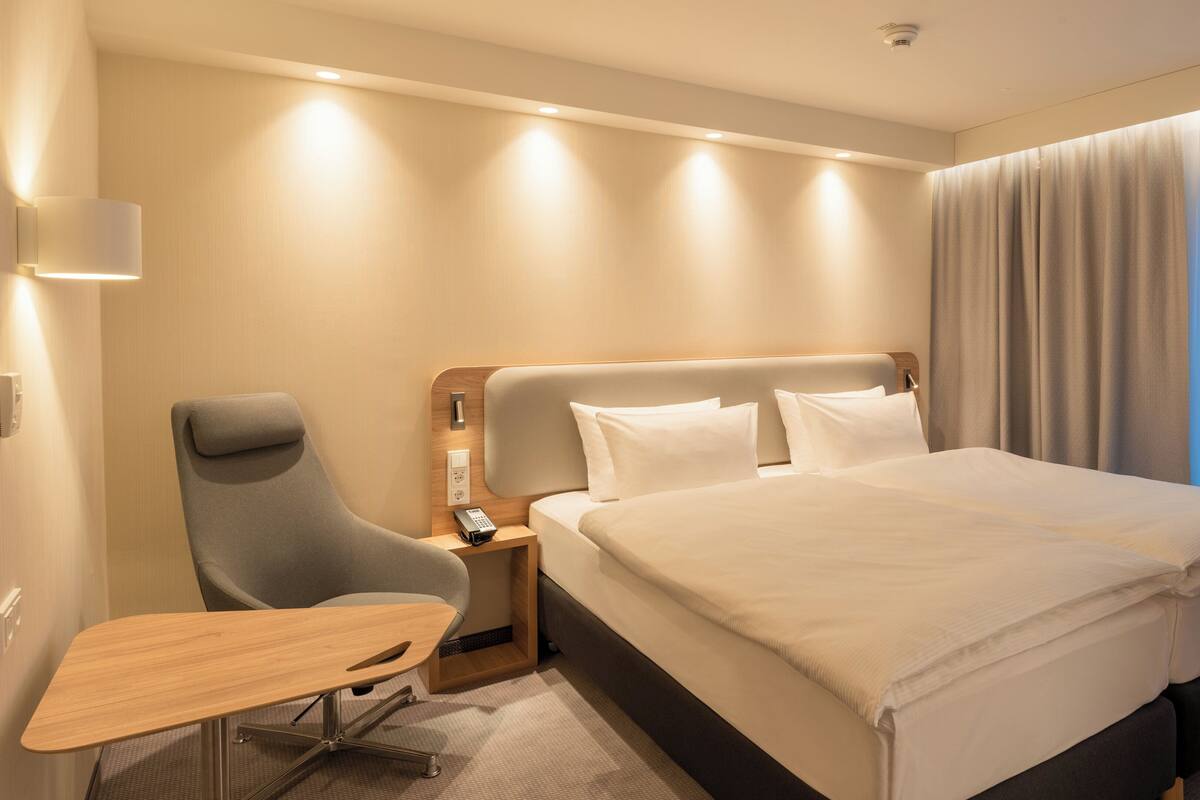 A hotel room with a bed, bedside table, chair, and a small desk.