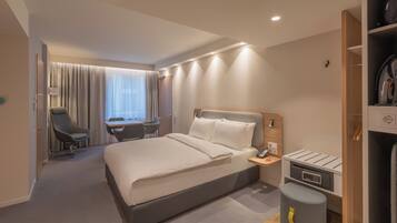 A hotel room with a bed, desk, chair, and a small seating area.