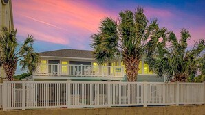 A two-story house with a balcony, surrounded by palm trees, under a colorful sky. - Vitamin Sea | Second-Row House | Private Pool (North Myrtle Beach)