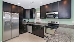 A modern kitchen with stainless steel appliances, dark cabinetry, and a granite countertop. - Vitamin Sea | Second-Row House | Private Pool (North Myrtle Beach)