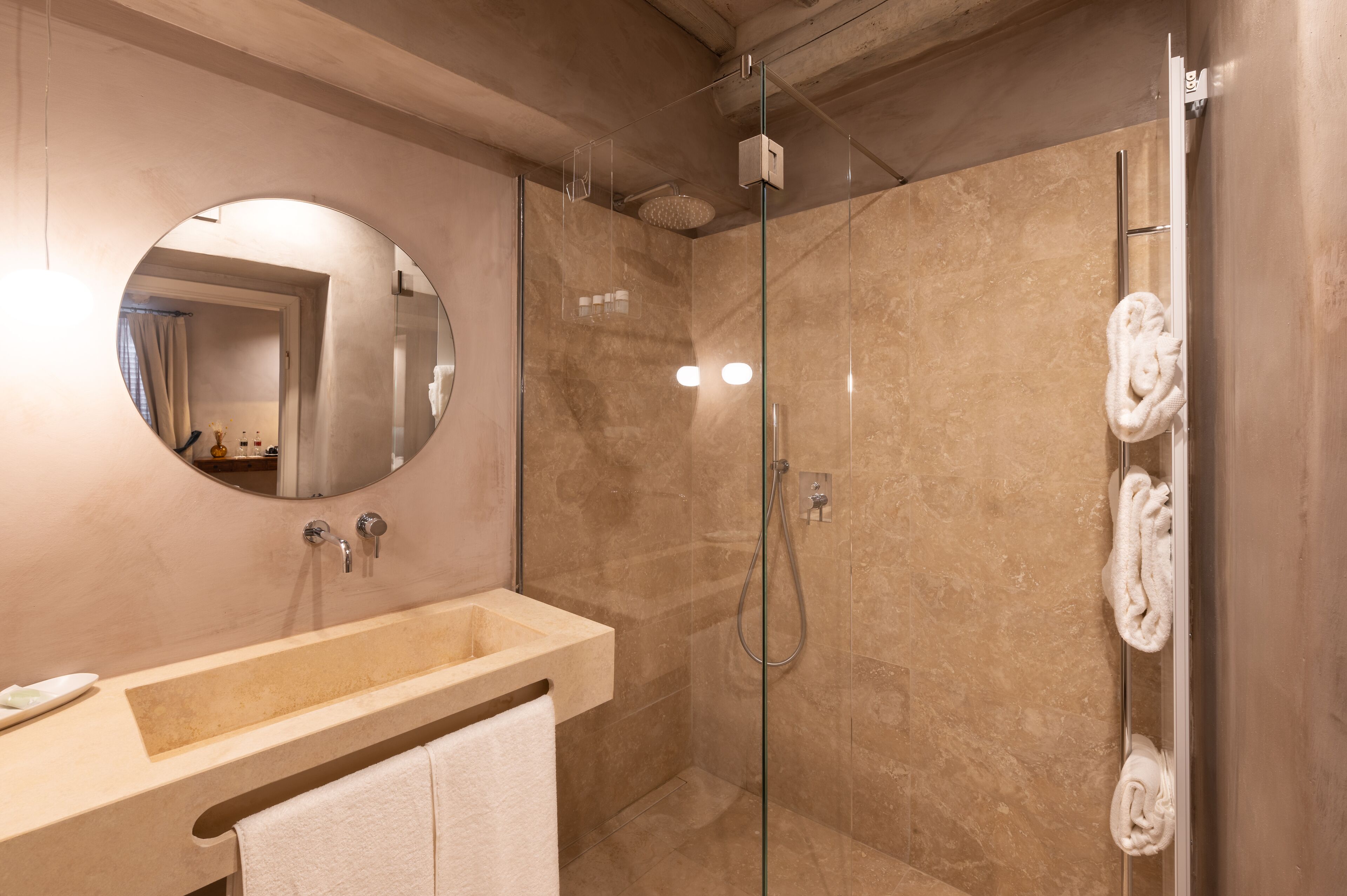 A modern bathroom with a glass-enclosed shower, a round mirror, and a beige vanity with a towel rack.