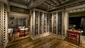 Una cava de vinos con estanterías de madera y mesas, un letrero que dice "DROGHERIA" y un techo rústico.