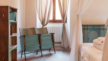 Ein Schlafzimmer mit einem Bett, einem Sessel, einem Bücherregal und einem Fenster mit Vorhängen.
