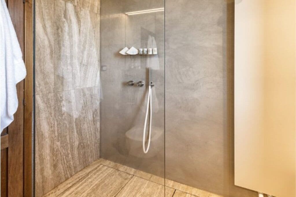 Un baño moderno con cabina de ducha de vidrio, suelo de madera y una toalla colgando a la izquierda.