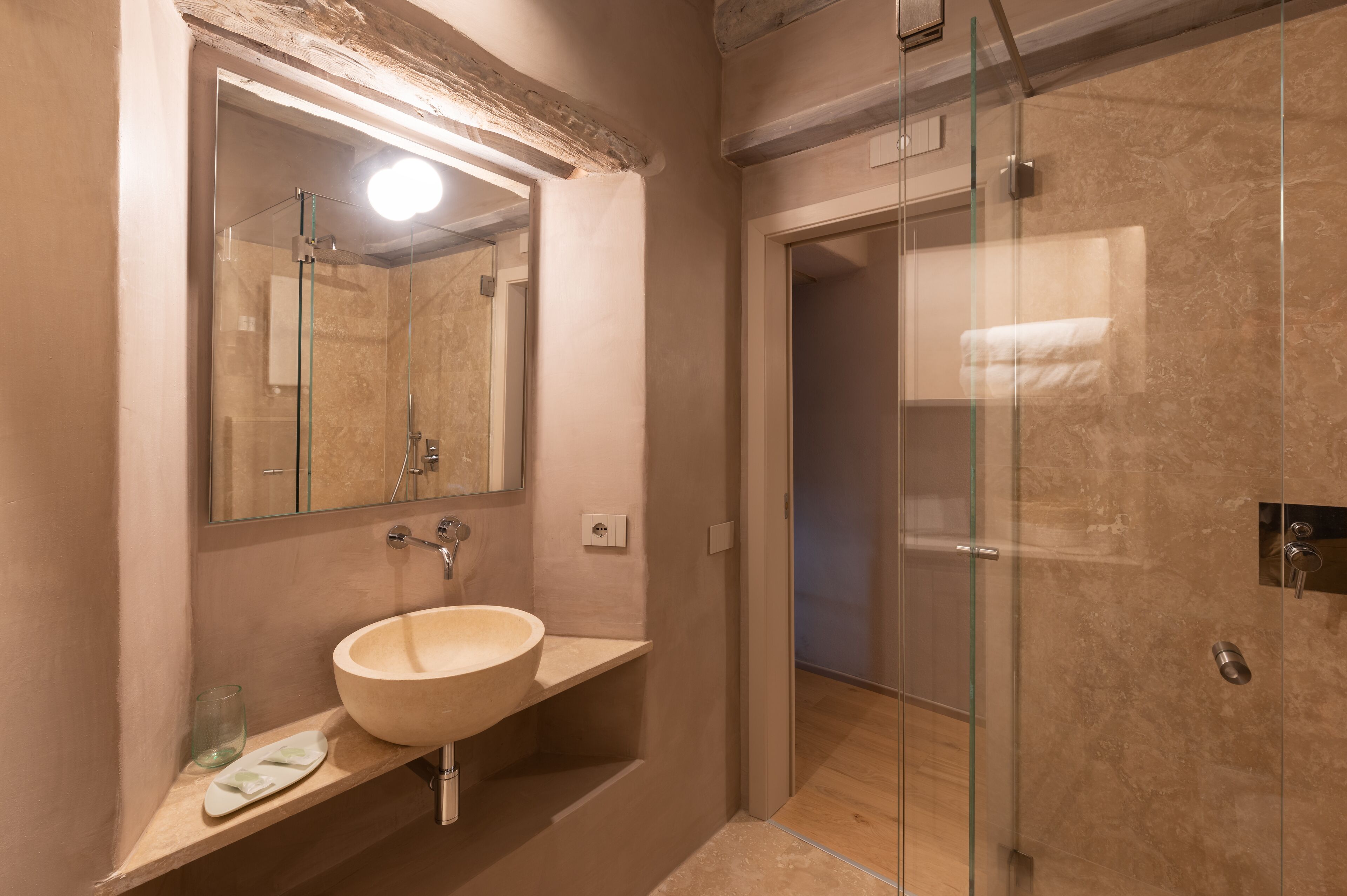 A modern bathroom with a large mirror, a beige sink, and a glass-enclosed shower.