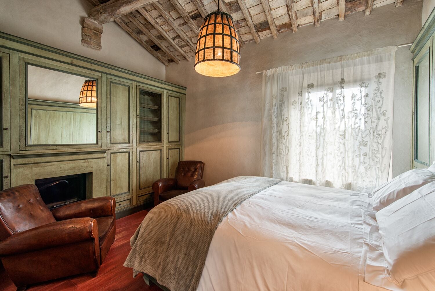 A bedroom with a large bed, a wooden chair, a television, and a fireplace.