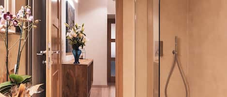 A modern bathroom with a glass-enclosed shower, a wooden vanity, and a vase of flowers.