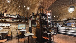 Un bar con paredes de ladrillo y estantes de madera llenos de botellas, mesas y sillas.