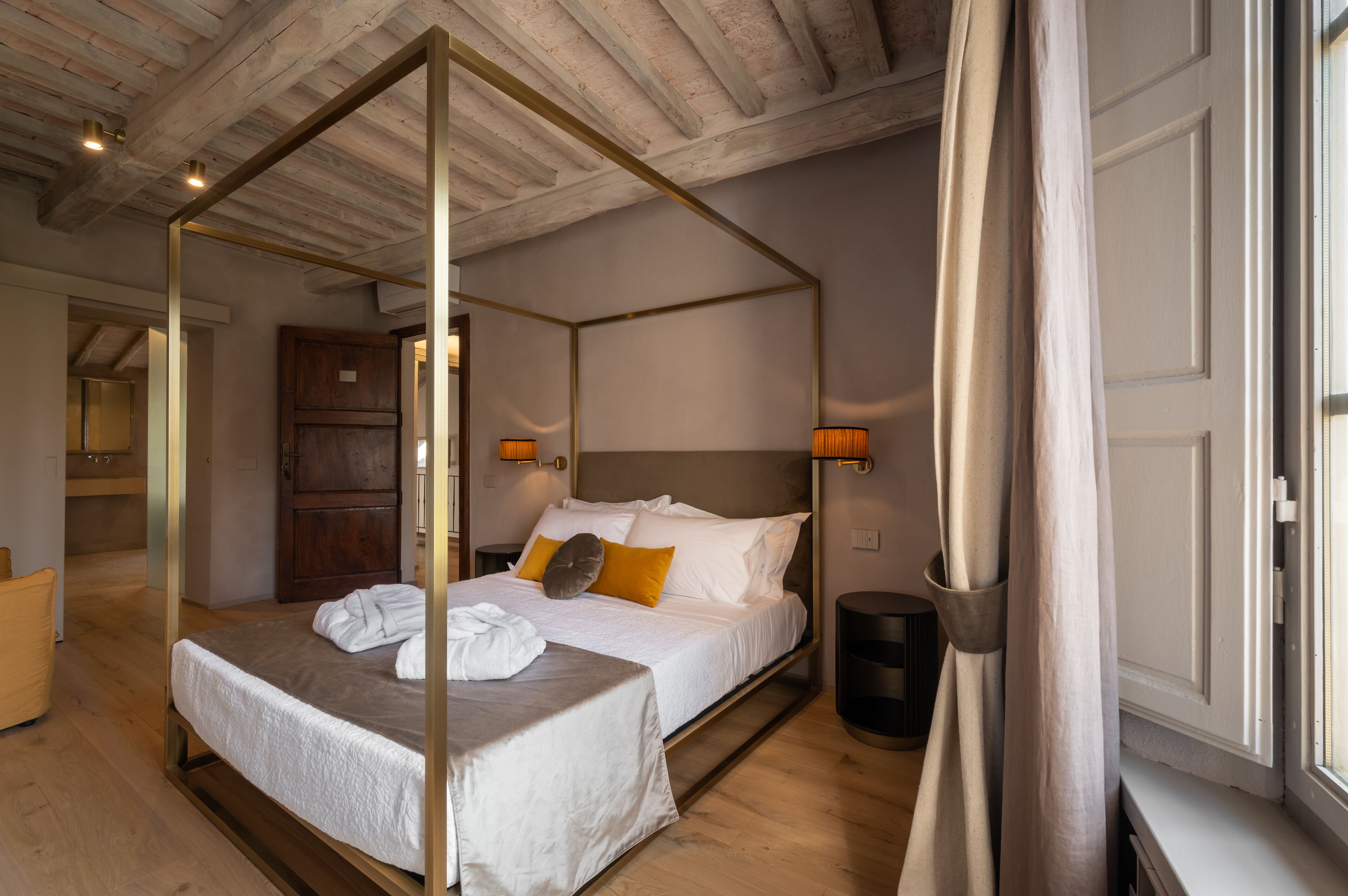 A four-poster bed with white linens, a wooden headboard, and a bedside table with a lamp.