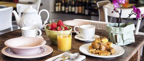 Una mesa de desayuno con una tetera, tazas, un cuenco de fresas, un vaso de jugo de naranja y un plato de comida.
