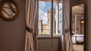 Un dormitorio con un ventanal grande que da a un castillo, una cama y un espejo en la pared.