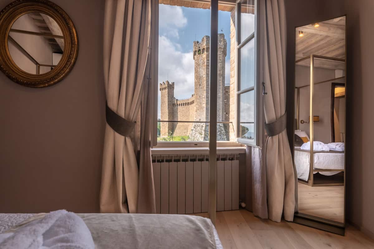 Un dormitorio con un ventanal grande que da a un castillo, una cama y un espejo en la pared.