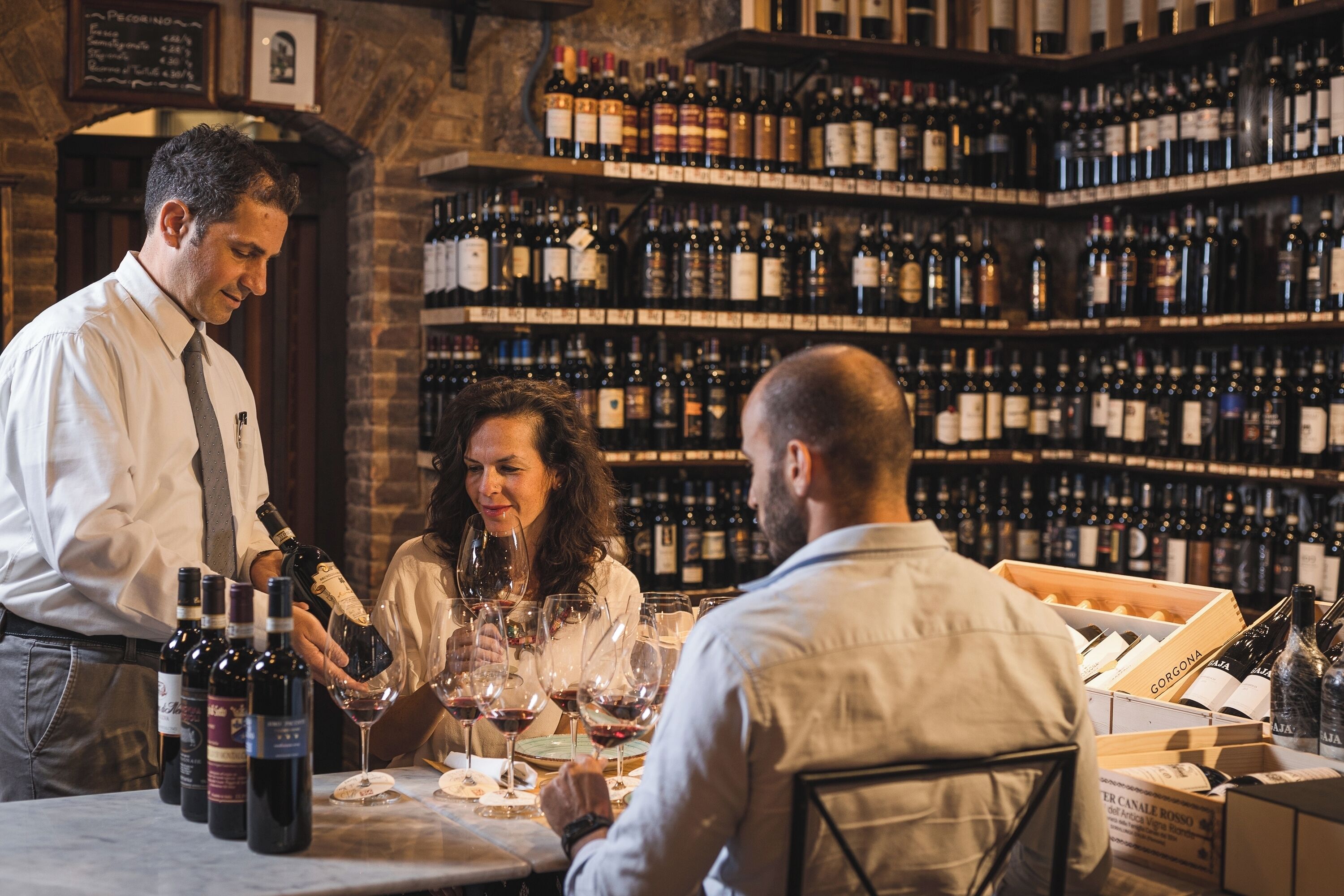 A bar with shelves of wine bottles and a table with wine glasses.