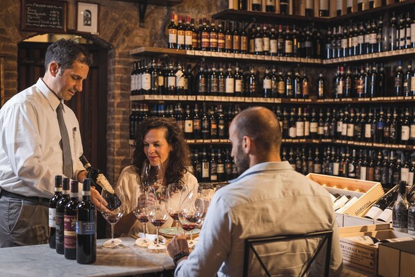 A bar with shelves of wine bottles and a table with wine glasses. - Casa Franci Montalcino  (Montalcino)