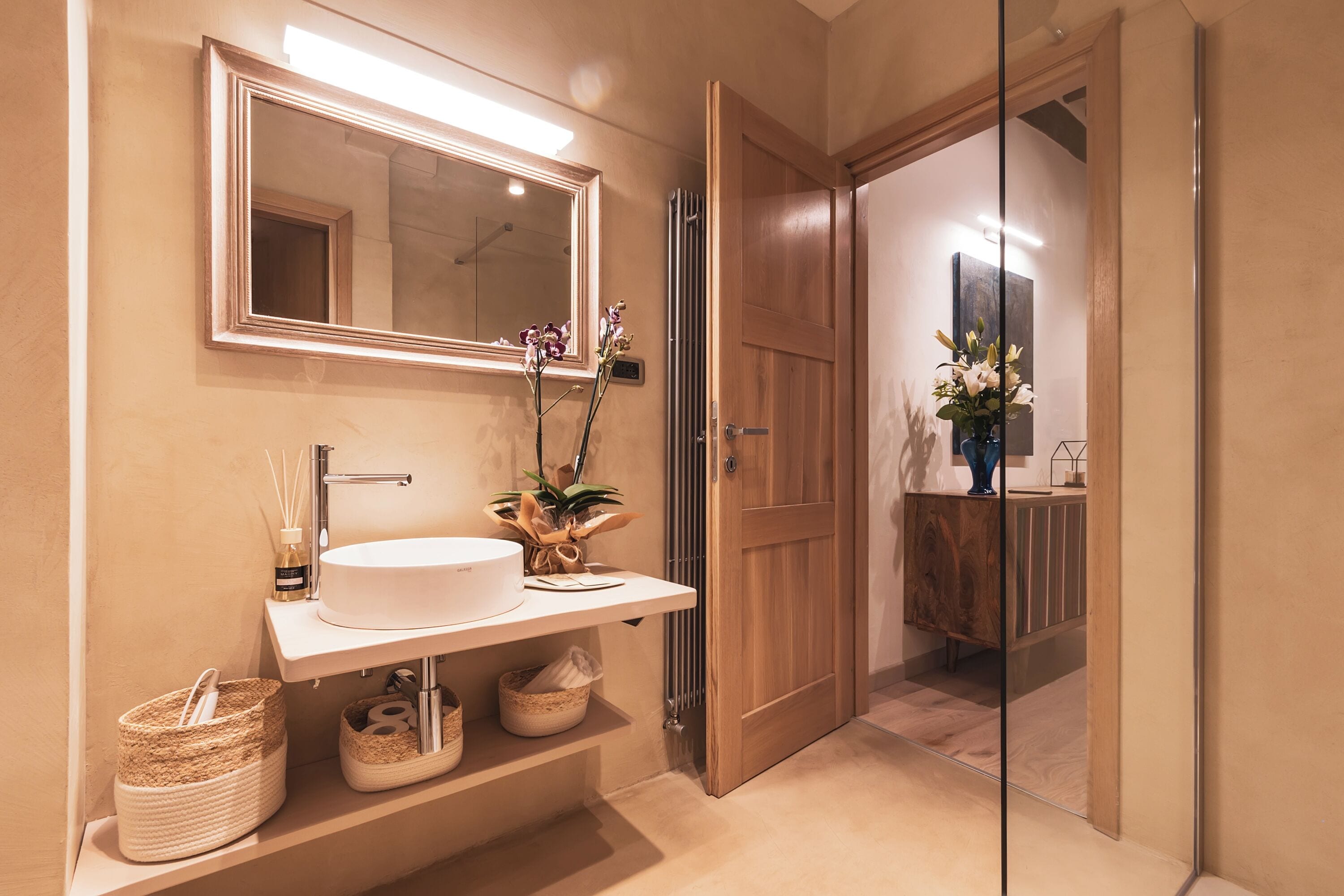 A modern bathroom with a large mirror, white sink, and wooden door.