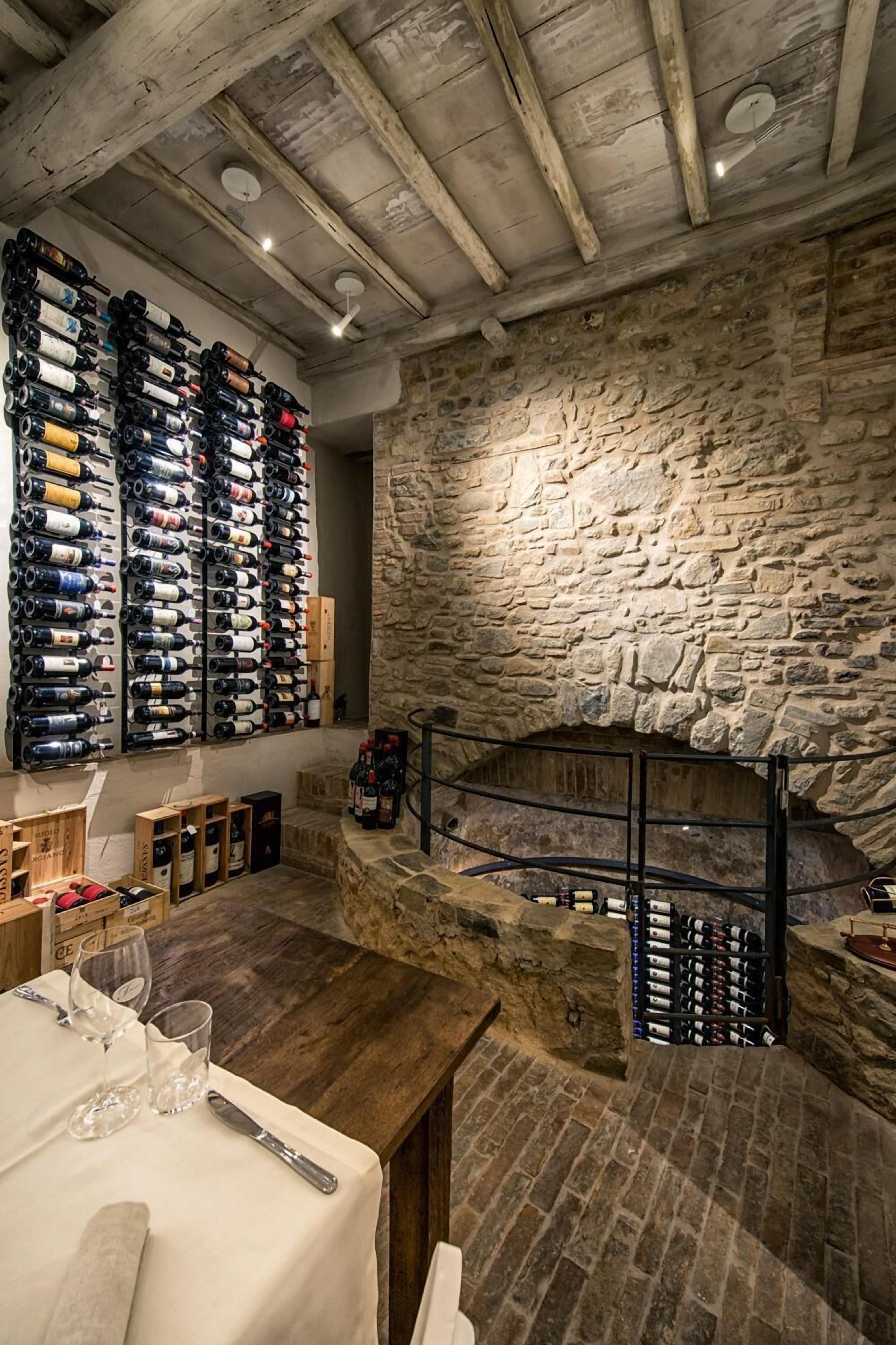 Une cave rustique aux murs de pierre, aux poutres en bois et à l’étagère à vin remplie de bouteilles.