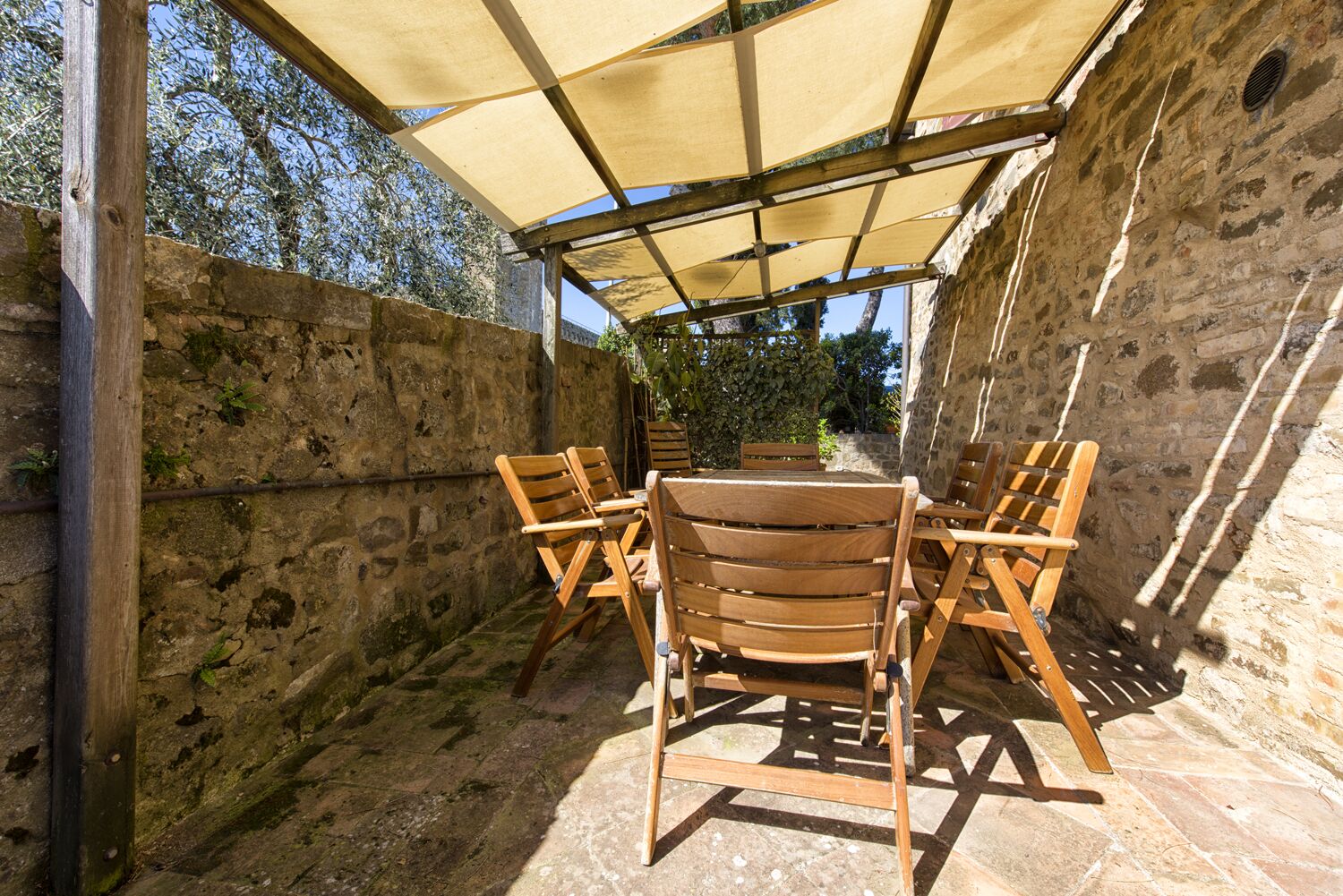 Un área de estar al aire libre con techo, paredes de piedra y una mesa con sillas.