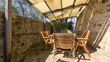 Un área de estar al aire libre con techo, paredes de piedra y una mesa con sillas.
