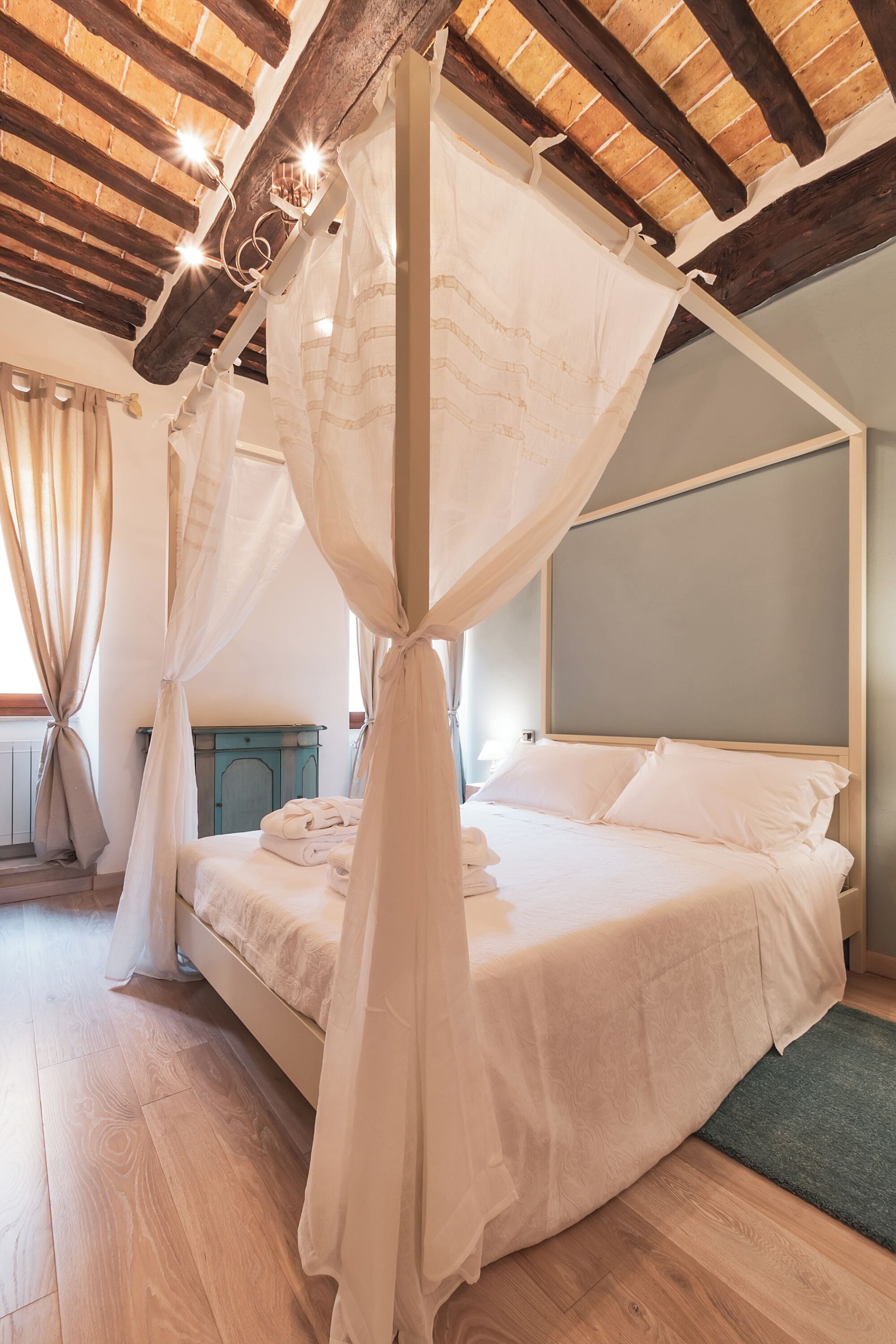 A bedroom with a four-poster canopy bed, wooden beams on the ceiling, and a small bedside table.