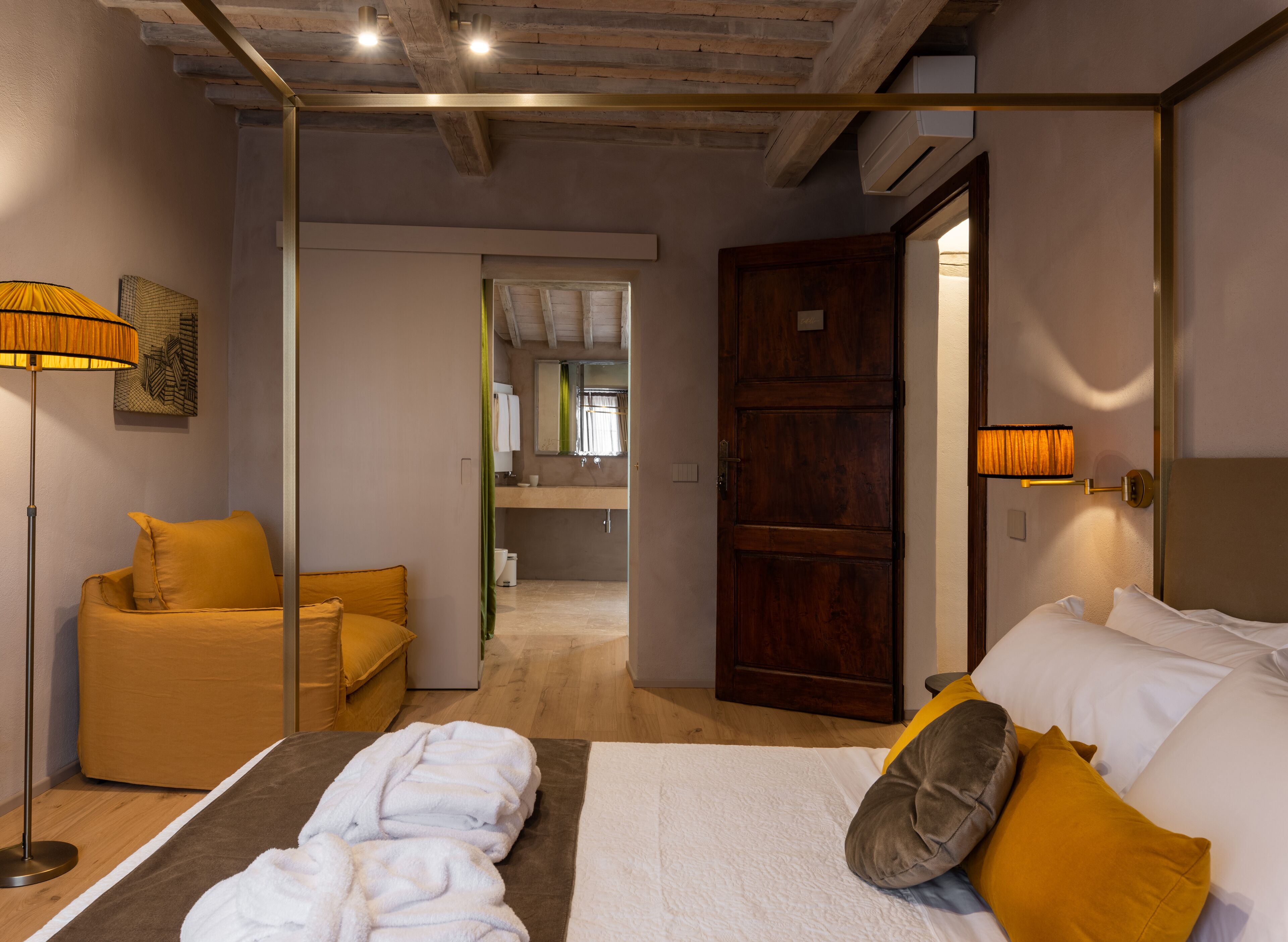 A modern hotel room with a bed, a sofa, a floor lamp, and a bathroom visible through an open door.