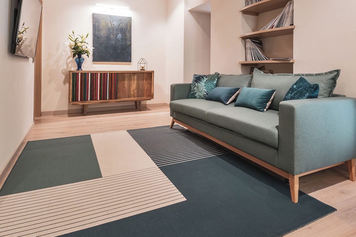 Una sala de estar moderna con vigas de madera a la vista, un sofá verde, una estantería y un cuadro abstracto grande en la pared.