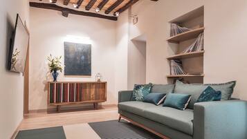 Una sala de estar moderna con vigas de madera a la vista, un sofá verde, una estantería y un cuadro abstracto grande en la pared.