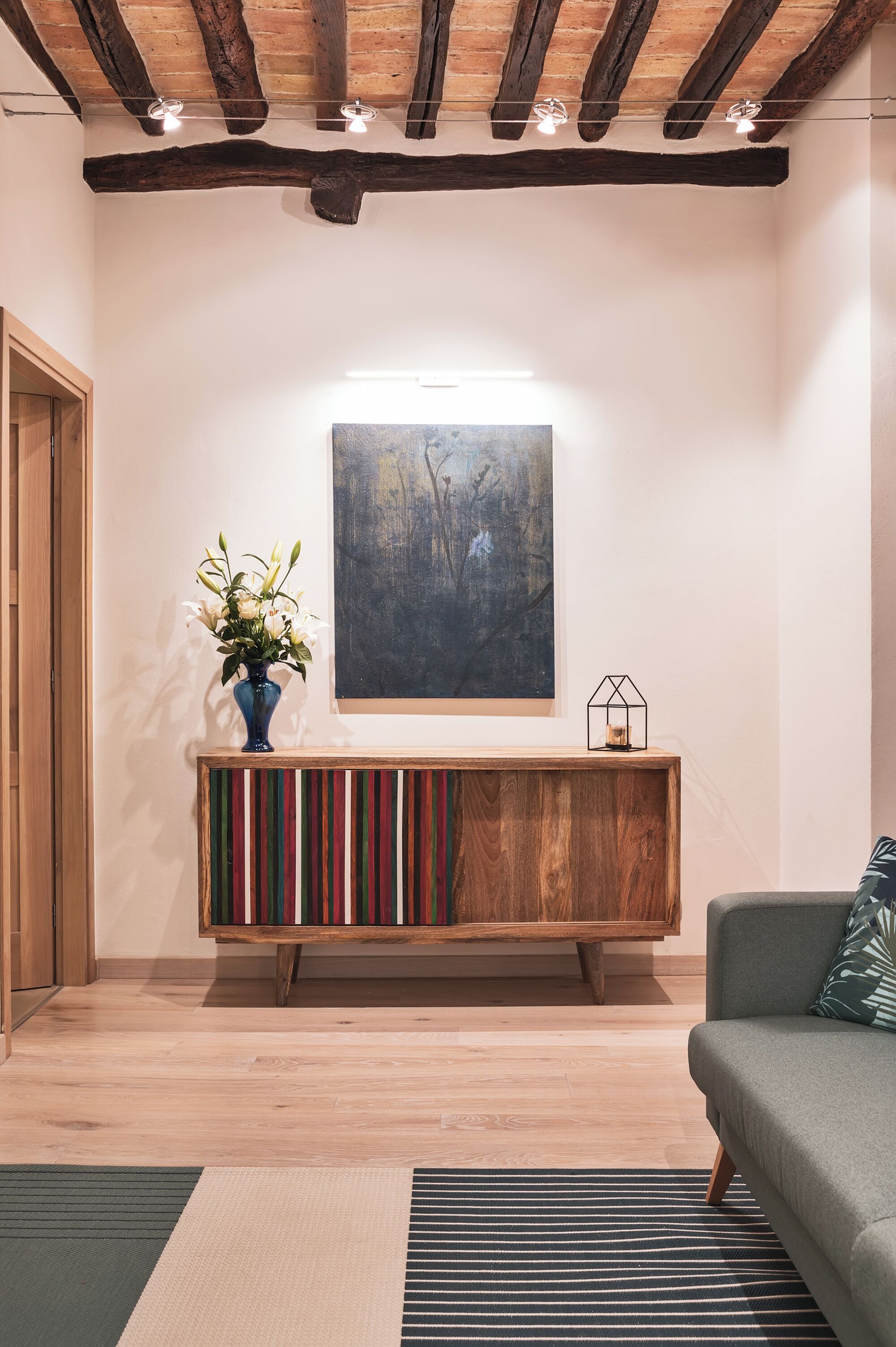 Una habitación con techo de madera, un cuadro en la pared, una consola con un florero y un sofá.