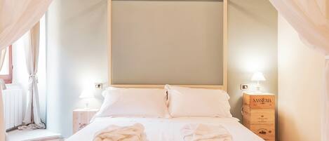 A bedroom with a canopy bed, white linens, two bedside tables with lamps, and a wooden chest of drawers.