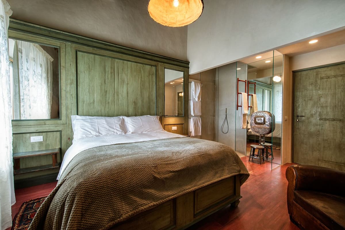 Un dormitorio con una cama grande, un cabecero de madera, un espejo, una silla de madera y un armario.
