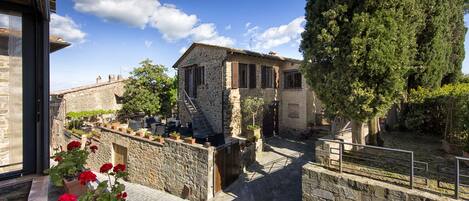 A stone building with a staircase leading to a door, surrounded by stone walls and potted plants.