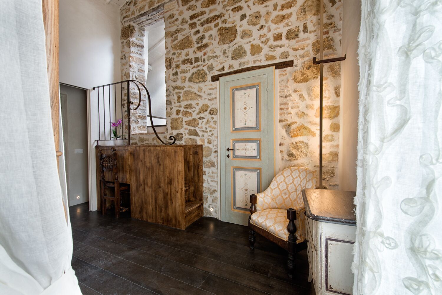 Una habitación con pared de piedra, un escritorio de madera, una silla y una puerta con paneles decorativos.