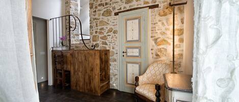 Una habitación con pared de piedra, un escritorio de madera, una silla y una puerta con paneles decorativos.