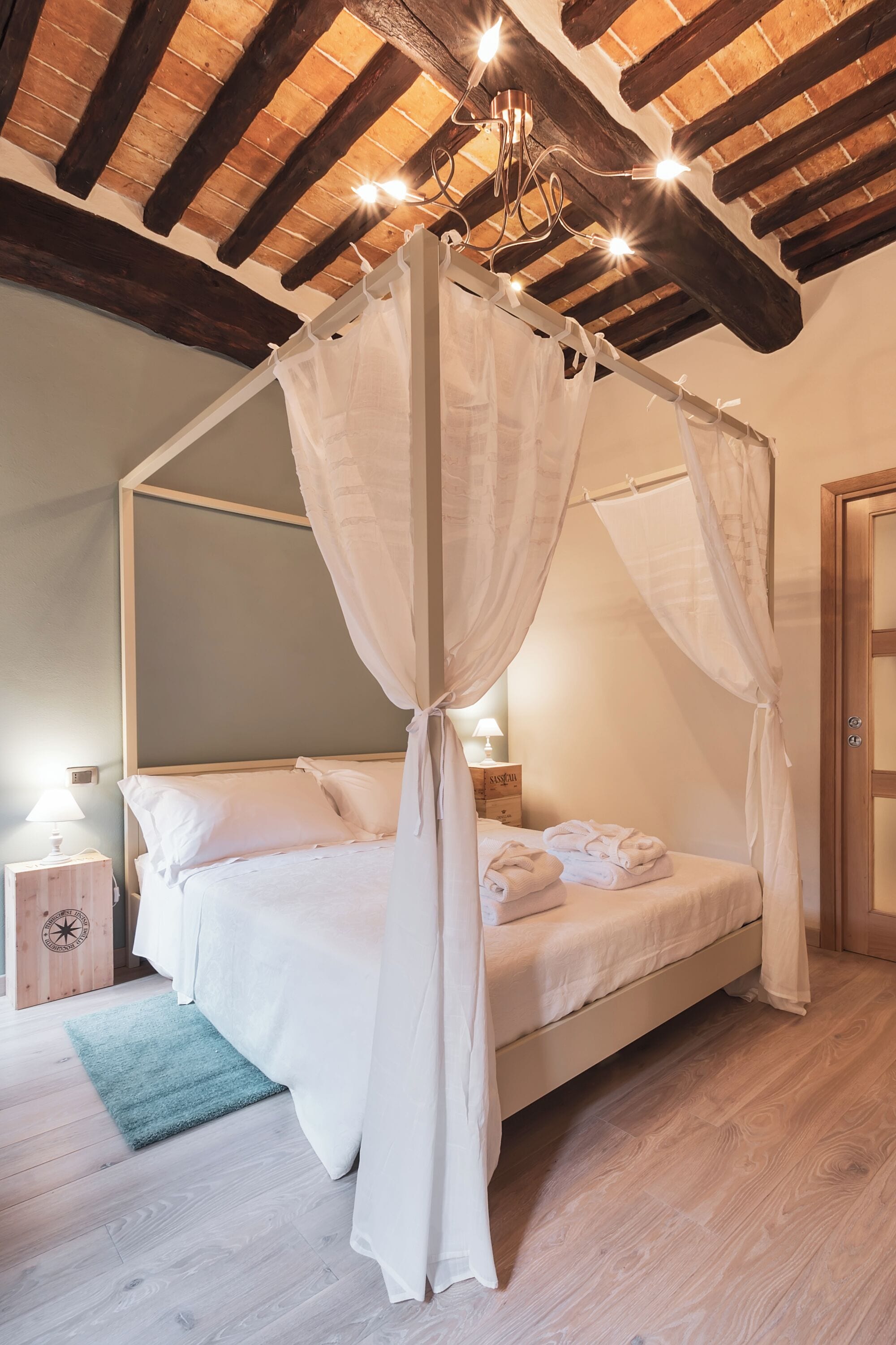 Un dormitorio con cama con dosel, vigas de madera en el techo y una mesita de noche con lámpara.