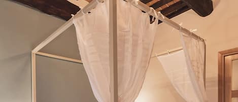 Un dormitorio con cama con dosel, vigas de madera en el techo y una mesita de noche con lámpara.